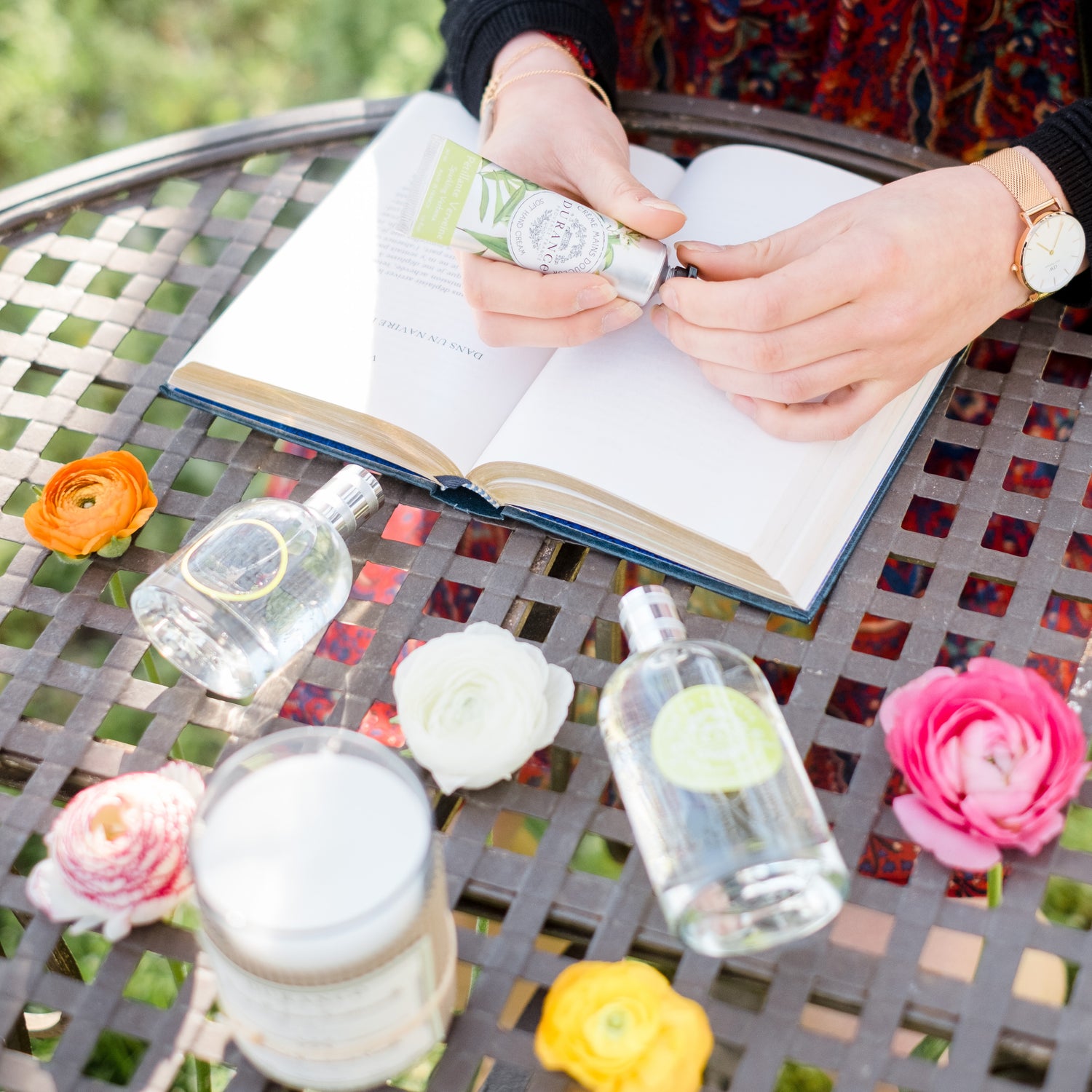 Woman with durance products putting on handcream in garden table outside with book open